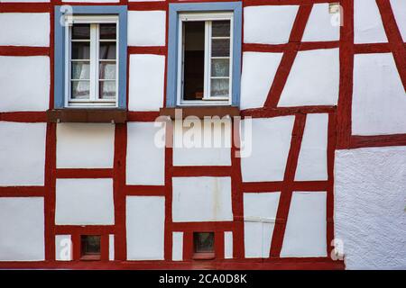 Mur blanc d'un ancien bâtiment à colombages avec poutres en bois rouge et cadres de fenêtres bleues Banque D'Images