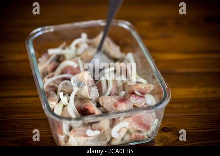 morceaux de hareng salé faits maison avec oignons et épices, sur une table en bois Banque D'Images