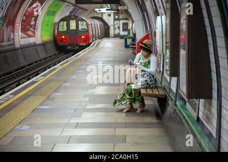 Femme d'âge moyen, portant une couverture faciale, un chapeau et une robe d'été, attendant un train de métro sur une plate-forme vide du métro de Londres. Londres, Angleterre Banque D'Images