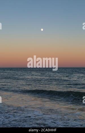 Une pleine lune visible au coucher du soleil, au-dessus de la mer à Brighton Banque D'Images