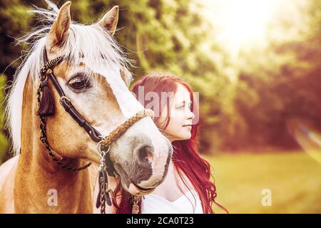 femme aux cheveux rouges avec cheval brun au coucher du soleil Banque D'Images