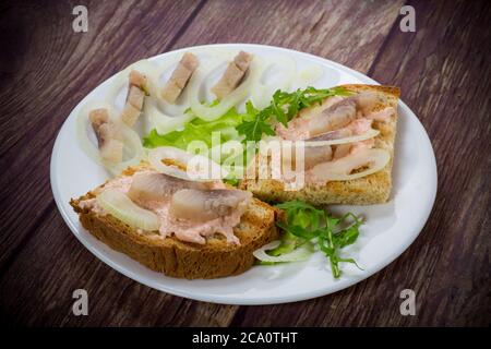 dans une assiette sur la table, faire un sandwich avec de la salade, du hareng et des herbes, avec des oignons Banque D'Images