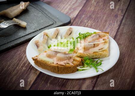 dans une assiette sur la table, faire un sandwich avec de la salade, du hareng et des herbes, avec des oignons Banque D'Images