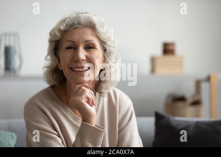 Une femme mûre s'assoit sur un canapé en souriant en regardant la caméra Banque D'Images