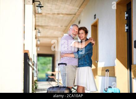 Couple senior avec bagages à l'extérieur de l'appartement en vacances, en vacances, en se serrant. Banque D'Images