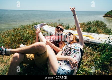 ODESSA, UKRAINE - MAI, 20 2015: Mignon jeune hipster couple de surfeurs avec surf faisant plaisir et plaisantant, couché sur l'herbe Banque D'Images