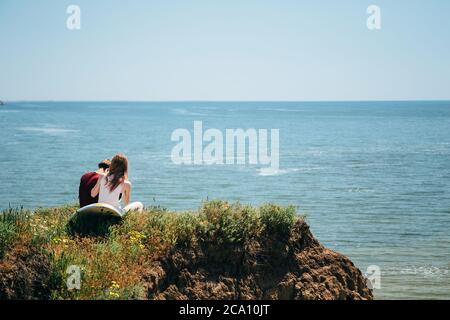 ODESSA, UKRAINE - MAI, 20 2015: Mignon jeune hipster couple de surfeurs avec surf assis sur la colline regardant la mer. Vue arrière Banque D'Images