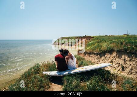 ODESSA, UKRAINE - MAI, 20 2015: Mignon jeune hipster couple de surfeurs avec surf assis sur la colline regardant la mer. Vue arrière Banque D'Images