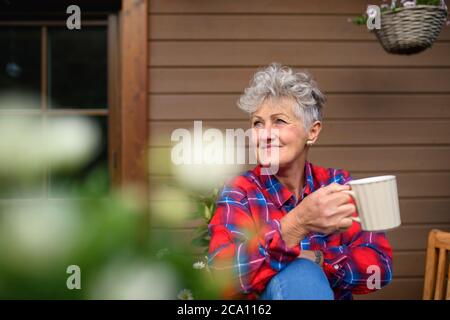 Femme âgée avec café assis sur la terrasse en été, au repos. Banque D'Images