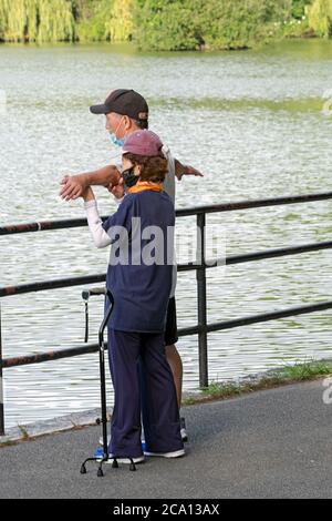 Un aide aide aide un homme ayant des problèmes de santé à faire sa routine d'étirement. Dans un parc à Flushing, Queens, New York. Banque D'Images