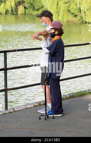 Un aide aide aide un homme ayant des problèmes de santé à faire sa routine d'étirement. Dans un parc à Flushing, Queens, New York. Banque D'Images