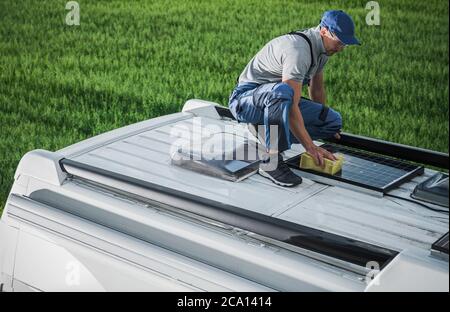 Caucasiens hommes dans son 40s nettoyage campeur Van RV toit installé panneaux solaires utilisant l'éponge et le détergent doux de lavage. Entretien des autocaravanes. Vösterstr Banque D'Images