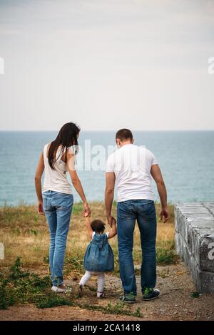 Jeune famille en t-shirts blancs et jeans bleus avec une petite fille en robe près du phare, vue arrière Banque D'Images