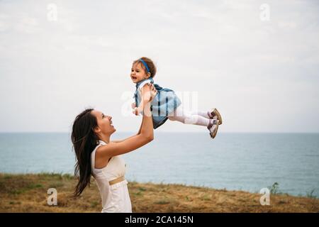 Bonne jeune mère jouant avec une petite fille, jetant dans l'air, à l'extérieur de l'arrière-plan Banque D'Images