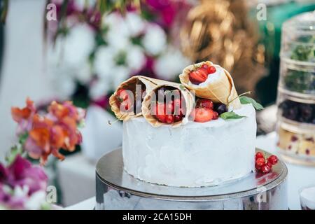 Délicieux gâteau blanc crémeux avec des cornets de gaufres remplis de différentes baies, entouré de décorations florales Banque D'Images