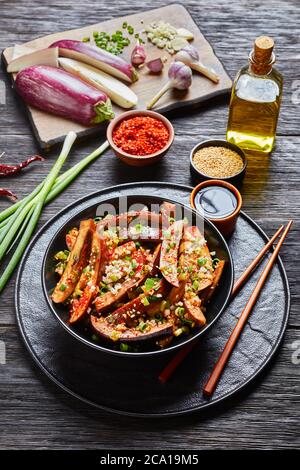 Gaji Namul, aubergine cuite à la vapeur et assaisonnée dans un bol noir sur une table en bois avec sauce soja et baguettes et ingrédients sur une planche à découper, coréen s. Banque D'Images