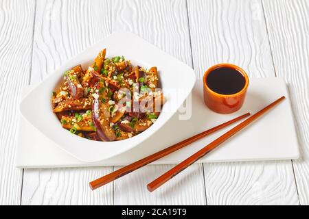 Gaji Namul, aubergine cuite à la vapeur et assaisonnée dans un bol blanc sur une table en bois avec sauce soja et baguettes, accompagnement coréen, gros plan Banque D'Images