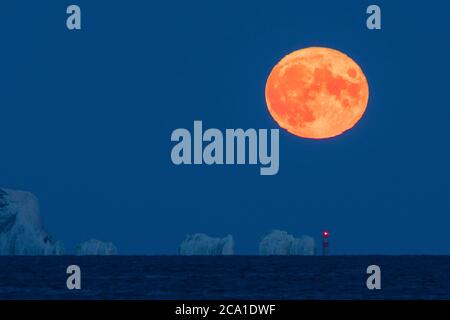 Mudeford, Dorset, Royaume-Uni. 3 août 2020. Météo Royaume-Uni. La pleine lune d'esturgeon brille d'orange alors qu'elle s'élève de derrière le phare d'aiguilles sur l'île de Wight, vue depuis Mudeford Quay à Dorset, lors d'une soirée d'été claire. Crédit photo : Graham Hunt/Alamy Live News Banque D'Images