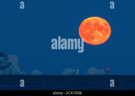 Mudeford, Dorset, Royaume-Uni. 3 août 2020. Météo Royaume-Uni. La pleine lune d'esturgeon brille d'orange alors qu'elle s'élève de derrière le phare d'aiguilles sur l'île de Wight, vue depuis Mudeford Quay à Dorset, lors d'une soirée d'été claire. Crédit photo : Graham Hunt/Alamy Live News Banque D'Images