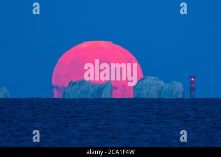 Mudeford, Dorset, Royaume-Uni. 3 août 2020. Météo Royaume-Uni. La pleine lune d'esturgeon brille de rouge alors qu'elle s'élève de derrière le phare d'aiguilles sur l'île de Wight, vue depuis Mudeford Quay à Dorset, lors d'une soirée d'été claire. Crédit photo : Graham Hunt/Alamy Live News Banque D'Images