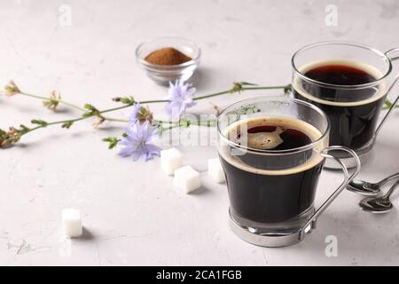 Boisson chicorée dans deux tasses en verre, avec concentré et fleurs sur fond gris. Boisson saine à base de plantes, succédané de café Banque D'Images