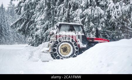 Tracteur déneigement des grandes bancs de neige à côté de la route forestière, après un blizzard en hiver Banque D'Images