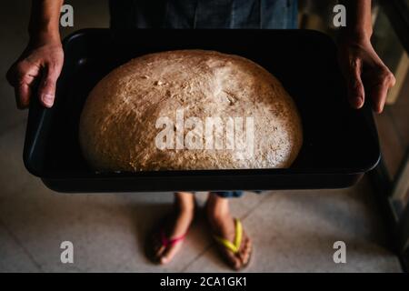 Mains de femme tenant une plaque de cuisson rectangulaire noire avec de la pâte fraîche brute pour le pain. Fait avec de la levure de fruits naturelle. Banque D'Images