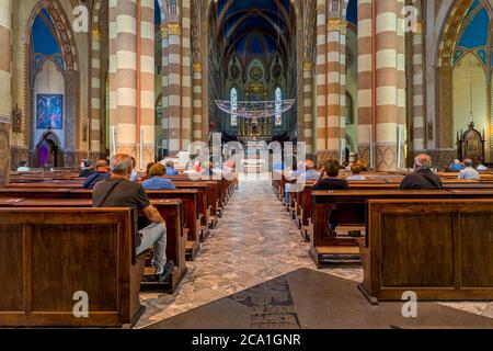 Les gens assis sur des ragoûts en bois pendant la messe à l'intérieur de San Lorenzo - une cathédrale catholique romaine alias Duomo à Alba, en Italie. Banque D'Images