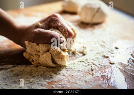 pétrissage à la main d'une pâte à farine en la faisant rouler sur une planche de bois. Préparation d'aliments à base de farine tels que pain ou pizza Banque D'Images