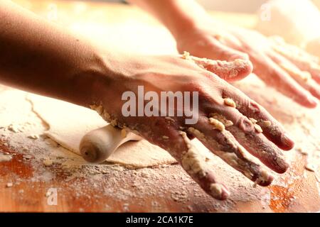 mains de femmes utilisant une broche de roulement pour paver une pâte sur une planche de bois sale avec de la farine. Préparation d'aliments à base de farine tels que pain ou pizza Banque D'Images