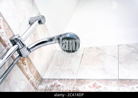 Intérieur d'une douche avec eau qui coule de la pomme de douche. Gouttelettes et humidité. Murs avec carreaux décorés. Hygiène et soins personnels Banque D'Images