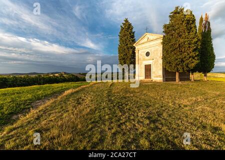 Vue panoramique de la légendaire chapelle de Vitaleta, au sommet d'une colline de Tuscanian, entourée de cyprès, sous un ciel bleu d'été avec des nuages rayés Banque D'Images