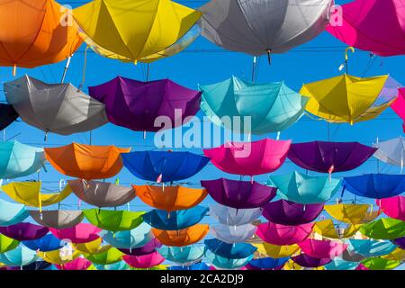 Des parasols colorés et dynamiques accrochés sur la rue piétonne pour un festival lors d'une journée ensoleillée au ciel bleu. Banque D'Images