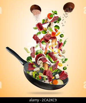 Légumes frais et morceaux de viande de bœuf volant dans une casserole, isolés sur fond marron. Concept de la nourriture volante, de la préparation, de l'alimentation et de la saine alimentation Banque D'Images