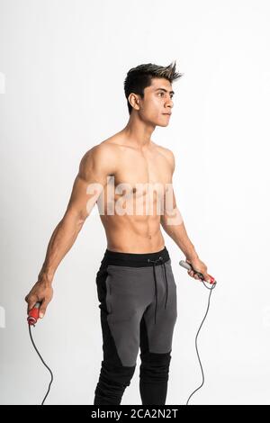 jeune homme avec corps musclé tenant une corde à sauter avec deux mains debout vers l'avant et regarder sur le côté sur un arrière-plan isolé Banque D'Images
