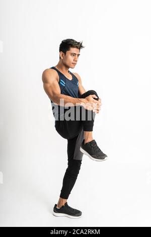 image du corps entier de l'homme de muscle portant des supports de sportswear face sur le côté, tendez la jambe en la soulevant vers l'intérieur face de l'estomac sur un fond isolé Banque D'Images