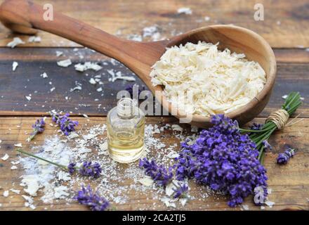 cuillère pleine de flocons de savon avec huile essentielle et bouquet de fleurs de lavande sur fond de bois Banque D'Images