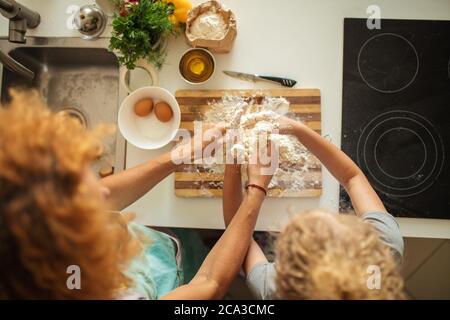 Vue à grand angle de la femme et de l'enfant fille les mains de fille faisant de la pâte verser l'huile d'olive dans le tas de farine . Nourriture maison et petit assistant. Banque D'Images