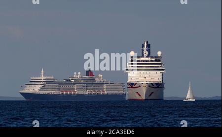 Un yacht passe devant les navires de croisière Queen Elizabeth (à gauche) et Arcadia, ancrés à Poole Bay au large de la côte du Dorset, tandis que les compagnies de croisière suspendent temporairement leurs opérations en raison de la pandémie du coronavirus. Banque D'Images