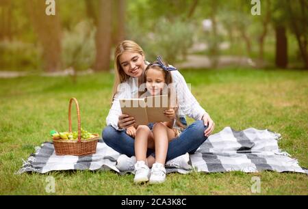 Amour maman et fille lecture livre Bonding ayant pique-nique à l'extérieur Banque D'Images