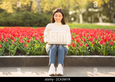 Fille asiatique utilisant un ordinateur portable, assis sur un parapet Banque D'Images