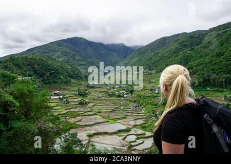 Femme blonde avec sac à dos en profitant des vues sur les rizières dans les montagnes à un point de vue de randonnée à Banaue, aux Philippines Banque D'Images