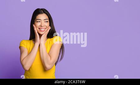 Offre incroyable. Curieuse fille asiatique regardant de côté et touchant le visage dans l'excitation Banque D'Images