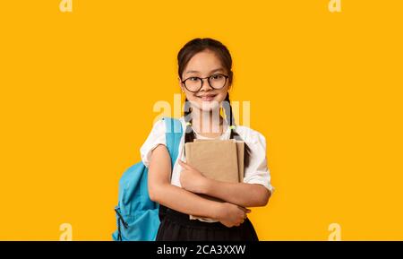 Gai Japanese School Girl hugging livre debout sur fond jaune Banque D'Images