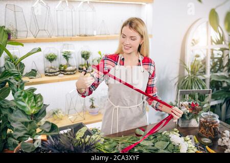 jeune jardinier attrayant au travail, prendre soin des plantes vertes, profiter de travailler avec des fleurs, isolé dans la salle pleine de fleurs et de plantes, le concept de botanique Banque D'Images