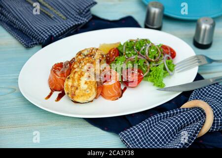 Des gâteaux de poisson avec salade, tomates et oignons rouges dans un restaurant sur une assiette blanche. Saumon rouge. Menu poisson. Gros plan. Nourriture saine Omega-3 sur bleu Banque D'Images