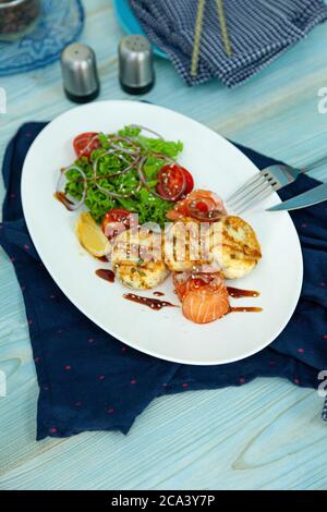 Des gâteaux de poisson avec salade, tomates et oignons rouges dans un restaurant sur une assiette blanche. Saumon rouge. Menu poisson. Gros plan. Nourriture saine Omega-3 sur bleu Banque D'Images