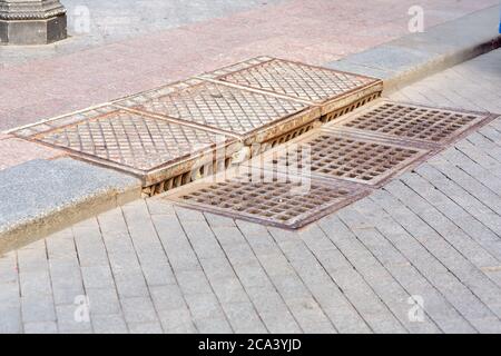 système de drainage carré pour trous d'homme douche tempête grille en fer sur le trottoir de la route avec trottoirs pour piétons. Banque D'Images