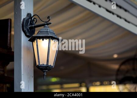 lanterne en fer noir avec verre dépoli et lumière chaude montée sur le pavillon en bois d'un café extérieur. Banque D'Images