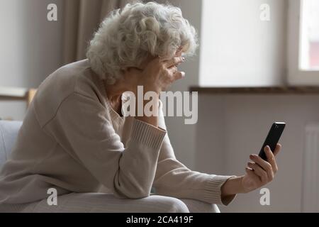 Une femme âgée tient un smartphone se sent déçue par les mauvaises nouvelles reçues Banque D'Images